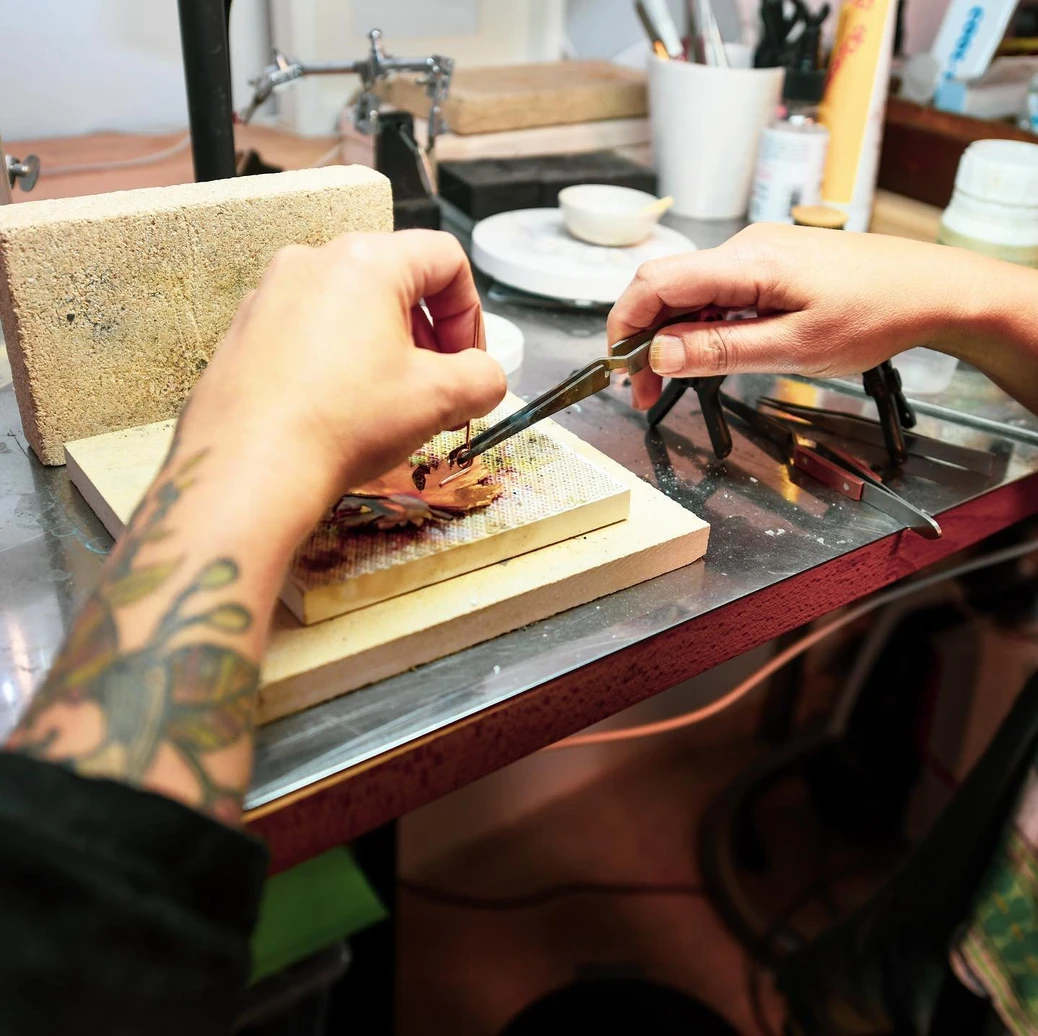 Gros plan sur les mains de l'artisane d'art Jane Bosshard-Quillerat façonnant minutieusement une pièce à l'établi de son atelier.