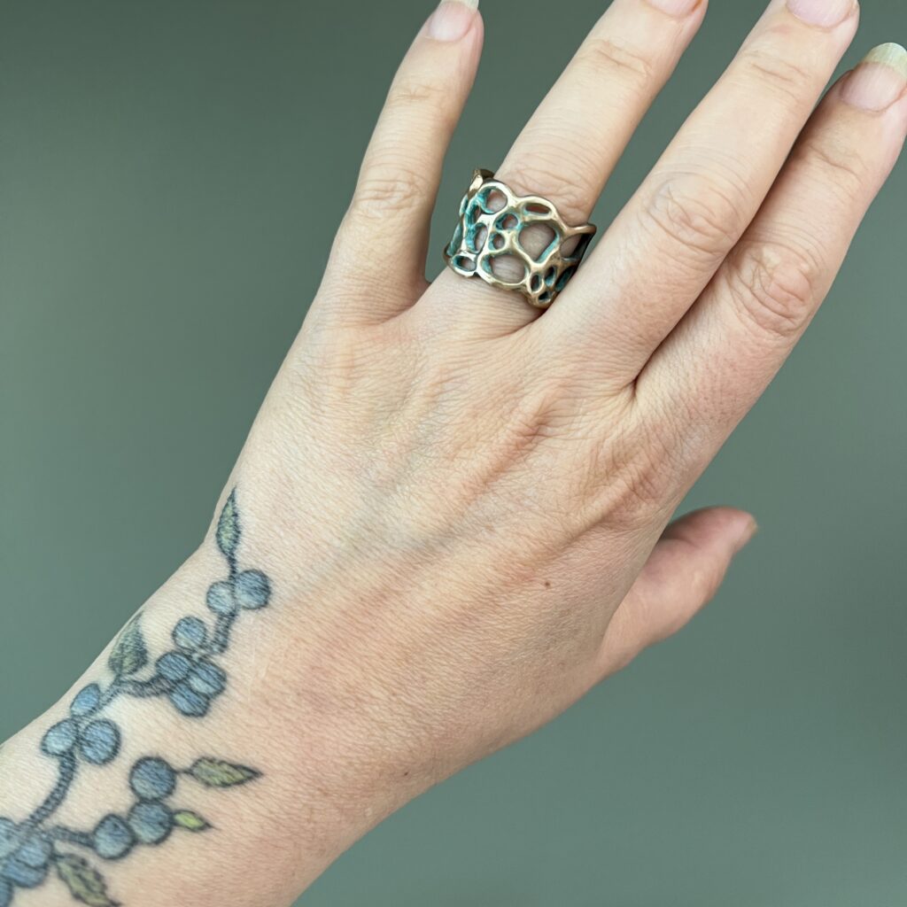 bague en bronze d'art de la collection Sculpture Sauvage de l'atelier Herbarium, porté à l'annulaire et photographié sur fond vert lichen