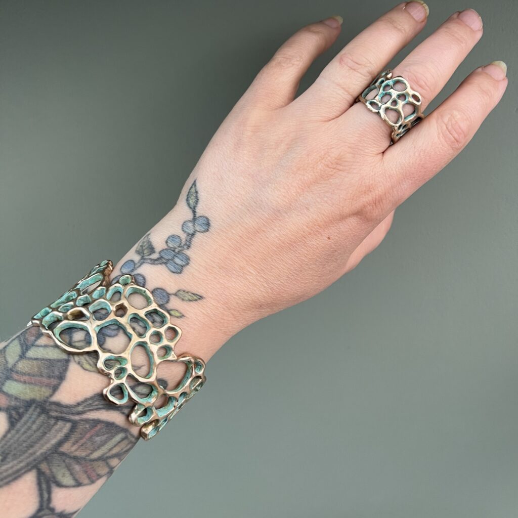 bague et bracelet en bronze d'art patiné au motif du lichen dentelle, de la collection Sculpture Sauvage de l'atelier Herbarium portés sur une main tatouée