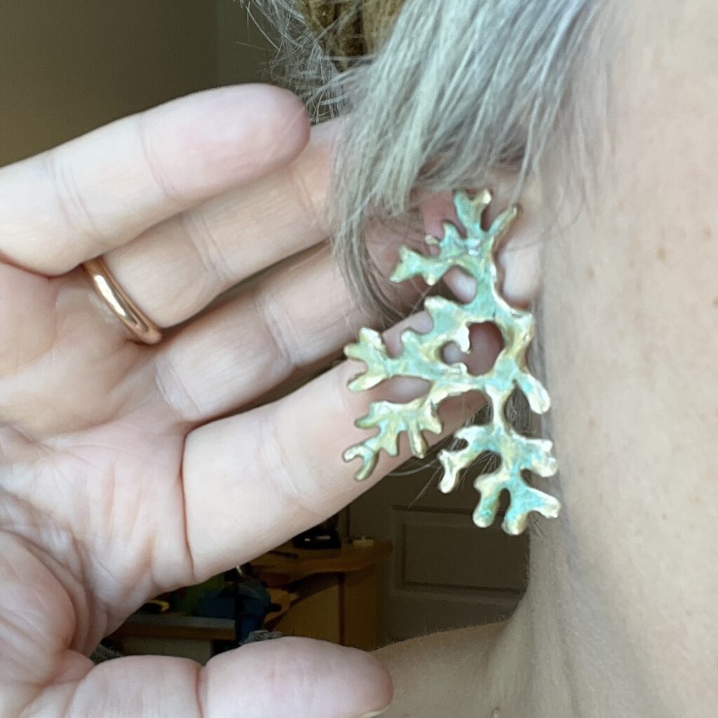 Boucles d'oreilles en bronze d'art patiné inspirée de la forme du lichen Mousse de chêne, portée sur un modèle photographié en gros plan. Collection Sculpture Sauvage de l'atelier Herbarium.