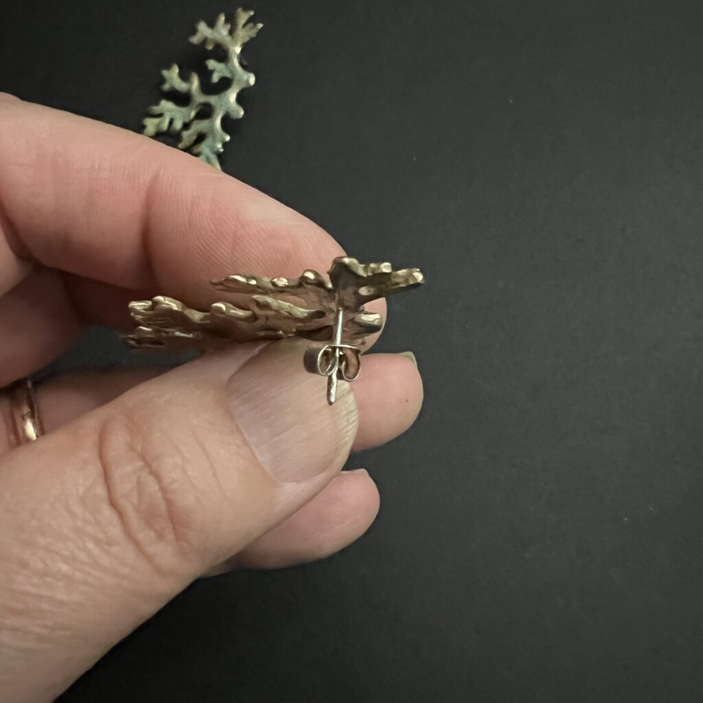 Détail d'une boucles d'oreille en bronze d'art patiné inspirée de la forme du lichen Mousse de chêne, présentée dans un main.